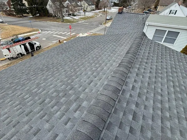 Newly shingled gray roof ridge above a residential street on a cloudy day