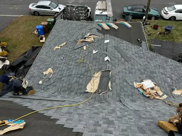 New gray shingles being installed course by course over black underlayment, seen from the top of the roof