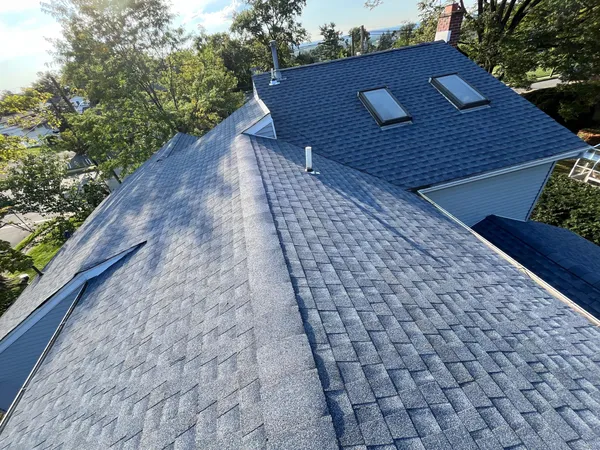 Completed roof replacement with blue-gray architectural shingles, two skylights, and a brick chimney