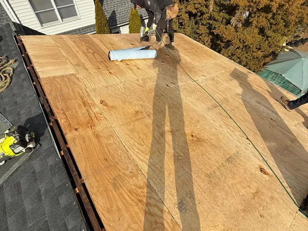 Roofer fastening new plywood decking to a stripped roof before underlayment goes on