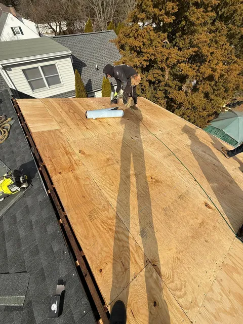 Roofer fastening new plywood decking to a stripped roof before underlayment goes on